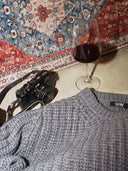 Gray sweater with 'Gobi' label, camera, and glass of red wine on a patterned rug. mobile