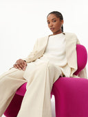 Woman in a beige suit sitting on a pink chair against a white background. mobile