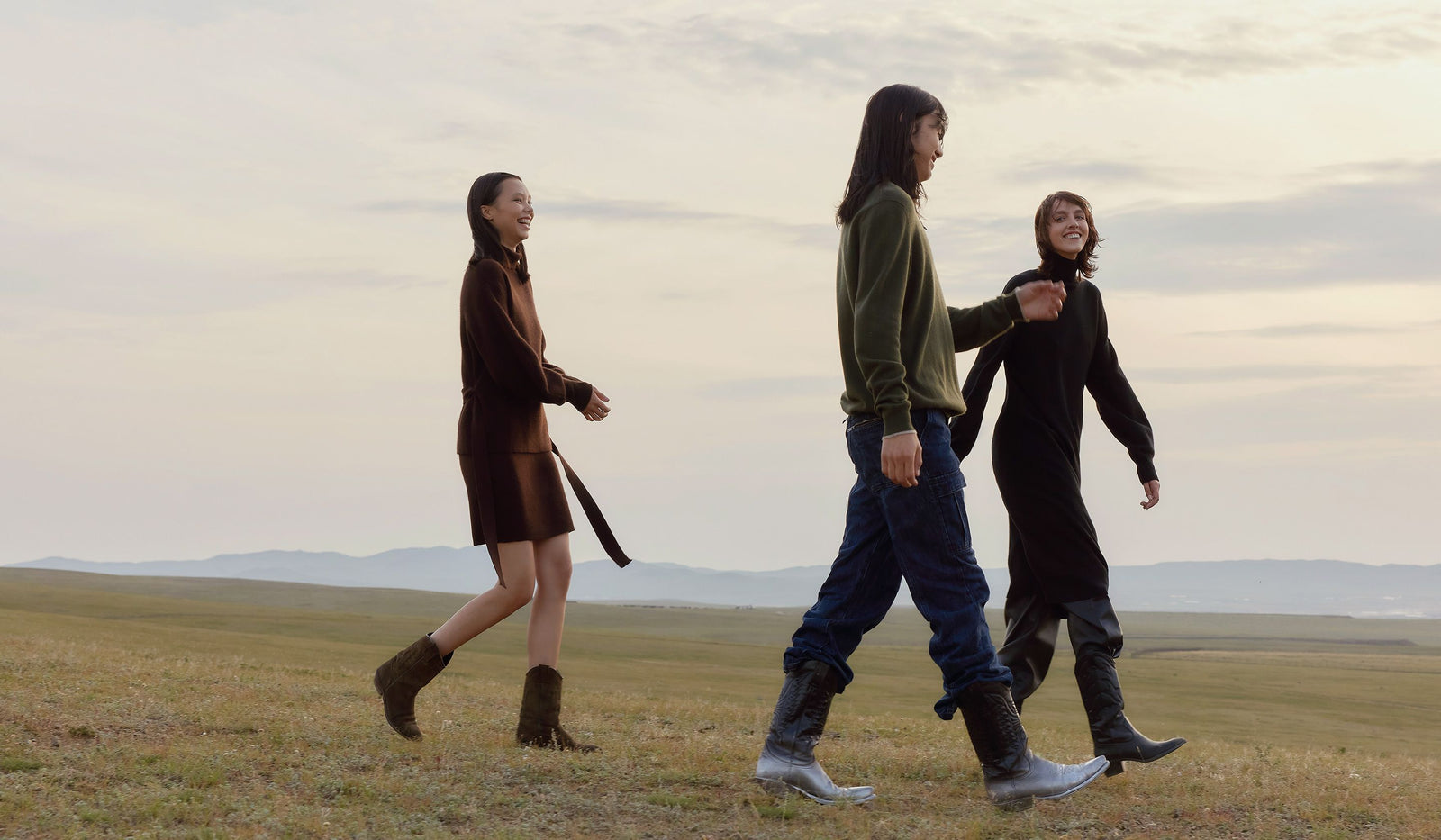 Three people walking together in a field with a scenic background. desktop