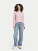 front view of a woman wearing a pink sweater and light blue jeans on a white background #color_almond-blossom