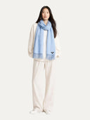 Woman wearing a light blue scarf with a brand logo on a white background #color_english-manor