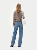 back view of a woman wearing a brown sweater and blue jeans, standing against a white background