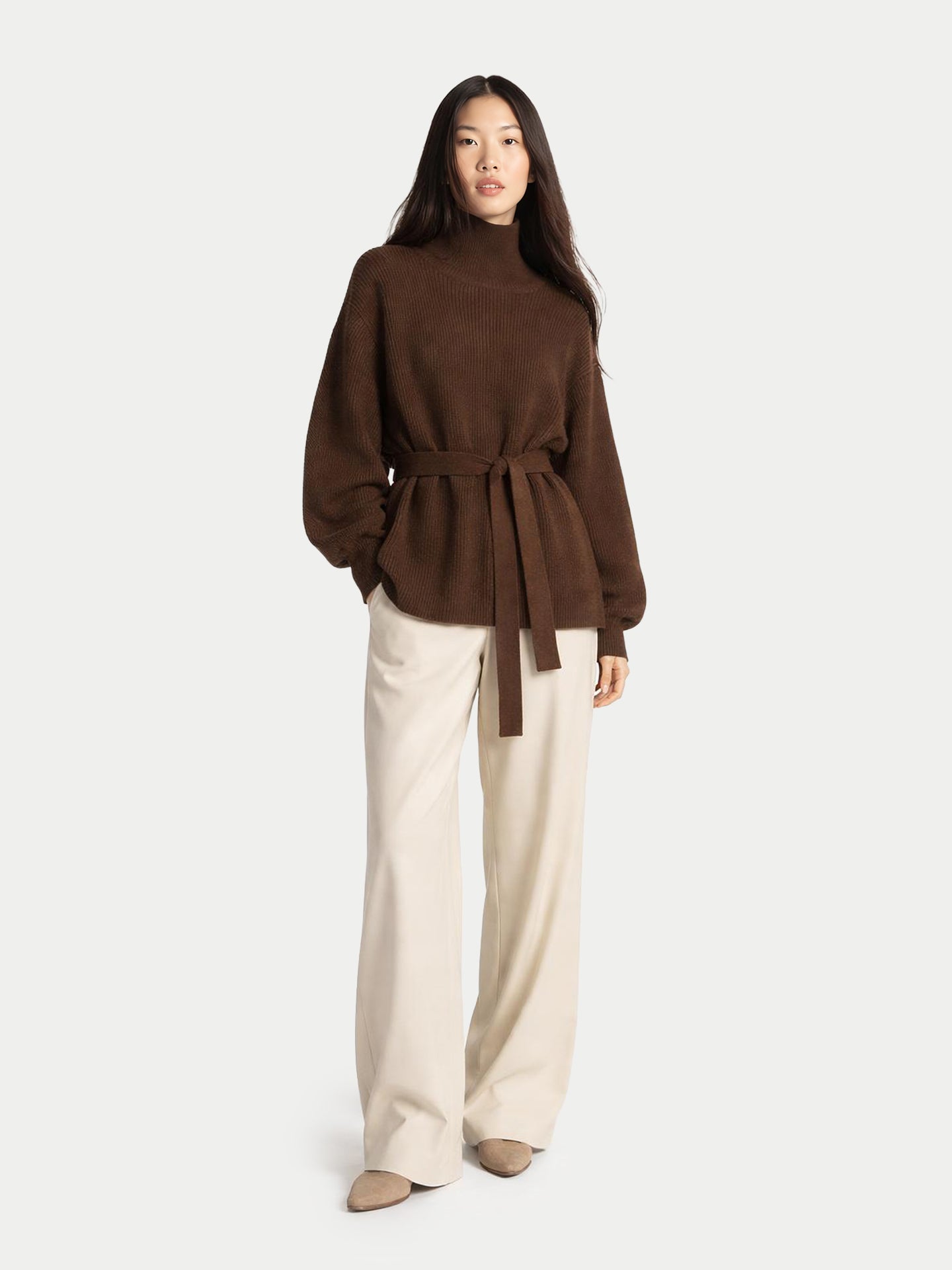 Woman wearing a brown belted top and beige pants on a white background