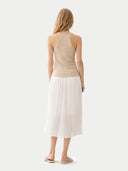 back view of Woman wearing a beige top and white pleated skirt on a light gray background #color_beige