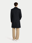 close up of a person wearing a black overcoat and beige pants on a white background #color_black