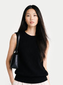 Woman wearing a black sleeveless top and holding a black handbag against a white background #color_black