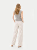 back view of a woman wearing a gray sleeveless sweater and white pants on a light gray background #color_dawn-blue