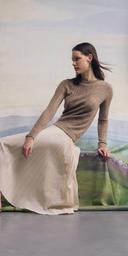 GOBI Cashmere Nomadic Summer campaign — woman in a beige pointelle-knit cashmere sweater and cream pleated skirt seated against a painted steppe landscape