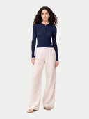 A woman modeling a navy blue ribbed long-sleeve top with a buttoned crew neck, paired with light beige wide-leg trousers, against a solid light gray background. #color_dark-indigo #ai-image
