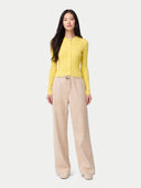 A woman modeling a bright yellow ribbed knit long-sleeve top with a front zipper and a pair of wide-leg beige trousers, standing against a light gray studio background.  #color_vivid-yellow