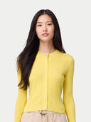 A woman with long dark hair wearing a bright yellow ribbed knit cardigan with a single button closure, paired with beige pants, against a light gray studio background. #color_vivid-yellow