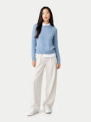 Woman wearing a light blue sweater and white pants on a white background #color_dusty-blue