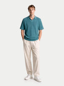 Man wearing a teal polo shirt and beige pants on a white background. #color_mineral-green