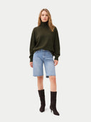 Woman wearing a green sweater, light blue denim shorts, and black boots on a white background #color_capulet-olive