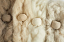 Four balls of undyed cashmere yarn — white, beige, warm grey and taupe — resting on raw cashmere fleece