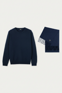 A navy blue crewneck sweater displayed next to a matching fringed scarf with a small embroidered logo, set against a plain light gray background. #color_navy
