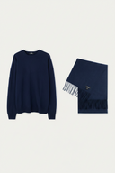 A navy blue crewneck sweater displayed next to a matching navy blue fringed scarf on a light gray background.