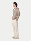 Person standing sideways wearing a beige hoodie and light-colored pants on a white background #color_taupe