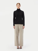 front view of a woman standing forward, wearing black turtle neck sweater and gray pants on a light gray background #color_black