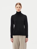 close up front view of a woman wearing black turtle neck sweater and gray pants on a light gray background #color_black