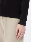 close up of a black sweater sleeve and gray jeans on a light gray background #color_black