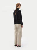 back view of a woman wearing a black turtle neck sweater and gray jeans on a light gray background #color_black