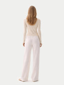 back view of a woman wearing a beige long-sleeve top and light pink pants on a white background. #color_pure-white