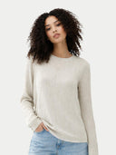 Woman wearing a beige sweater and light blue jeans against a white background #color_whisper-white