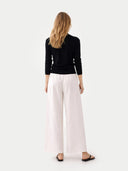 back view of a woman wearing a black top and white pants on a white background #color_black