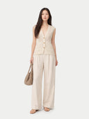 Woman wearing a beige sleeveless top and wide-leg pants holding a woven bag on a white background #color_off-white