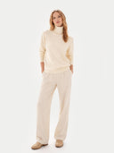 Woman wearing a cream turtleneck sweater and beige pants on a white background #color_off-white