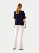 back view of a woman wearing a navy blue top and white pants on a light gray background #color_navy