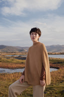 A woman in a camel cashmere poncho beside a wetland lake under a wide sky