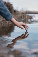 A hand in a blue cashmere sleeve touching the surface of a clear stream