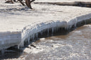 Icicles hanging from a snow-covered river bank over dark flowing water
