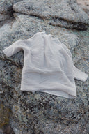 A cream ribbed cashmere knit laid on a lichen-covered rock