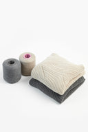 Cones of grey and cream cashmere yarn beside folded CashmeReborn sweaters