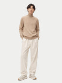 front view of a man wearing a beige turtleneck sweater and white pants on a white background #color_warm-grey