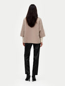 back view of a woman wearing a beige poncho and black pants on a white background #color_taupe