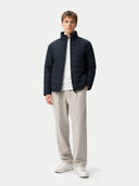 Man wearing a navy puffer jacket, white shirt, beige pants, and white sneakers on a light gray background #color_navy-blazer