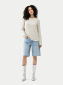 Woman wearing a beige sweater, light blue denim shorts, and silver boots on a white background #color_whisper-white