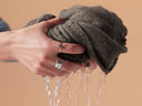 Person wringing out a dark gray towel with water dripping, against a beige background