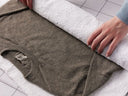 Person folding a gray garment on a white towel on a tiled floor