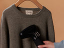 Brown sweater with 'Gobi' label being ironed by a hand holding a black iron against a beige background