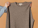 Person holding a gray sweater with 'Gobi' branding against a brown background
