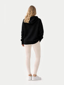 Back view of person wearing a black hoodie and white pants on a light gray background #color_black