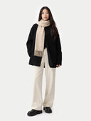 Person wearing a black coat, beige scarf, and white pants on a white background #color_warm-grey