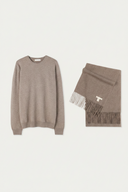 A taupe knit crewneck sweater and a matching fringed scarf with a small white monogram logo, displayed on a light off-white background.