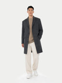 Man wearing a dark gray coat, beige sweater, white pants, and white sneakers on a white background #color_charcoal