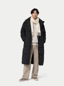 Person wearing a black puffer coat, beige scarf, and light gray pants on a white background #color_white